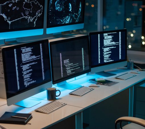 Workplace of contemporary it-engineers with three computers standing on desk in large openspace office